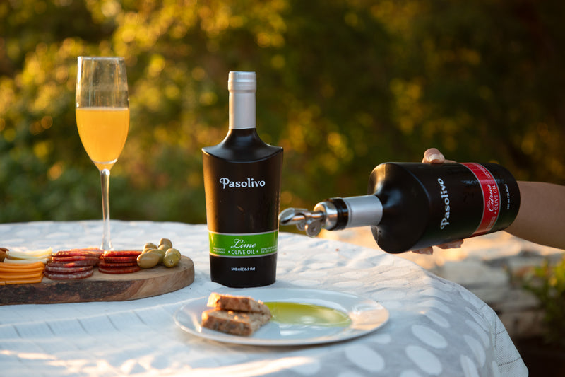 Person pouring a drink from a 'Pasolivo' bottle into a glass on a table outdoors.
