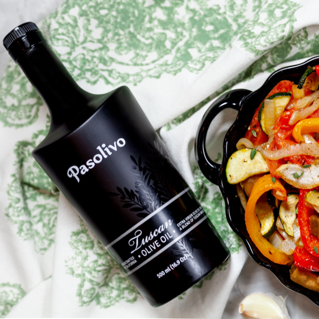 Bottle of Pasolivo Tuscan Olive Oil next to a dish of roasted vegetables on a patterned surface