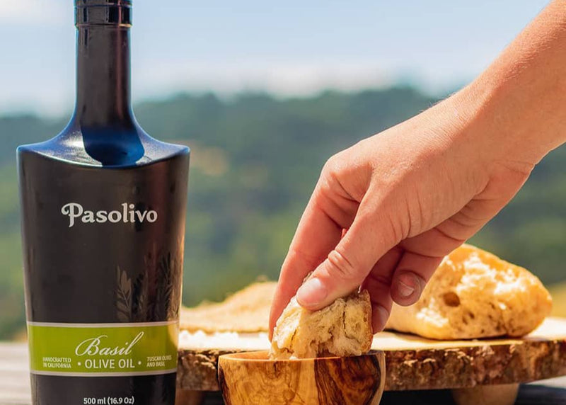 Bottle of Pasolivo Basil Olive Oil with a hand holding bread outdoors