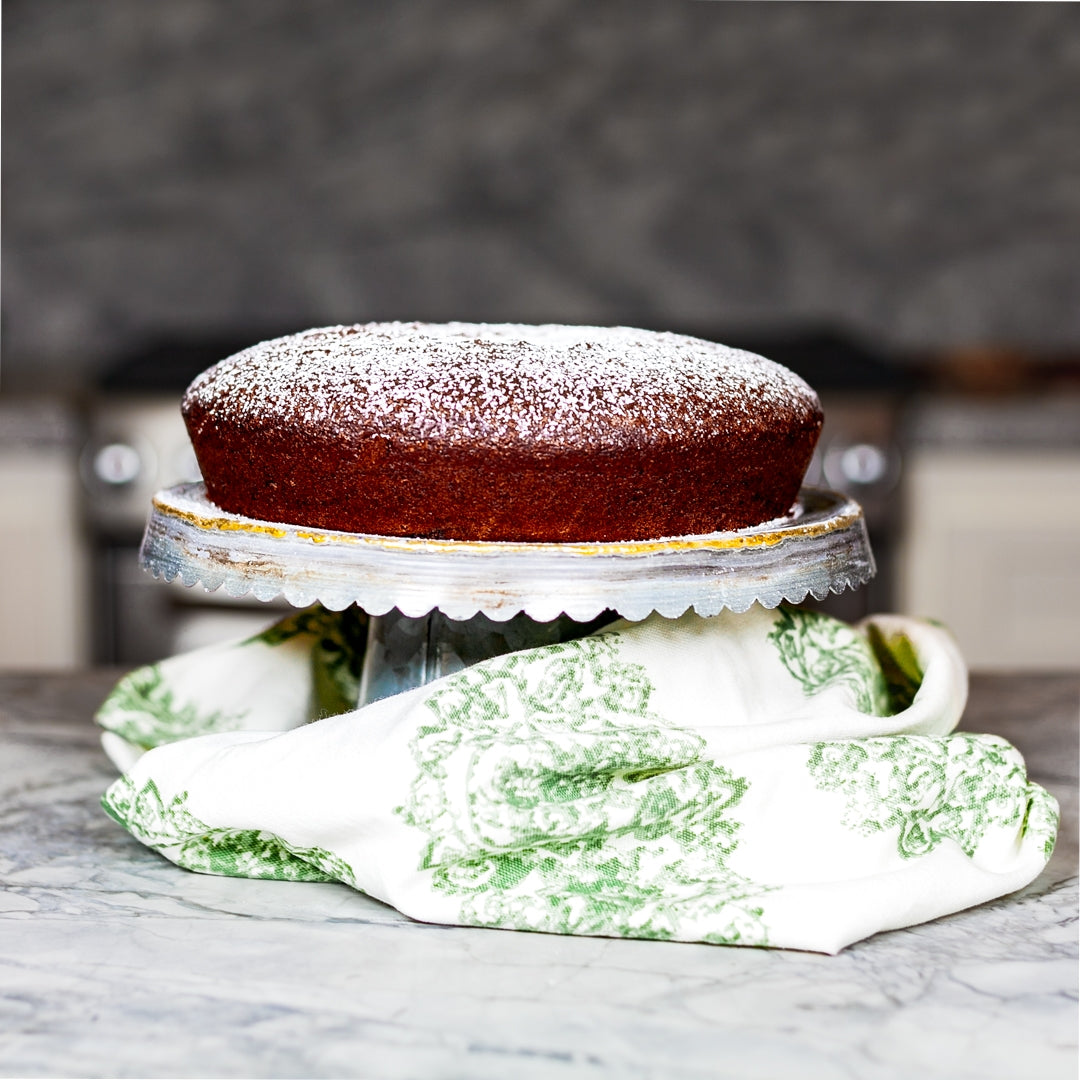 Chocolate Lemon Olive Oil Cake recipe resting on cake stand on top of marble countertop