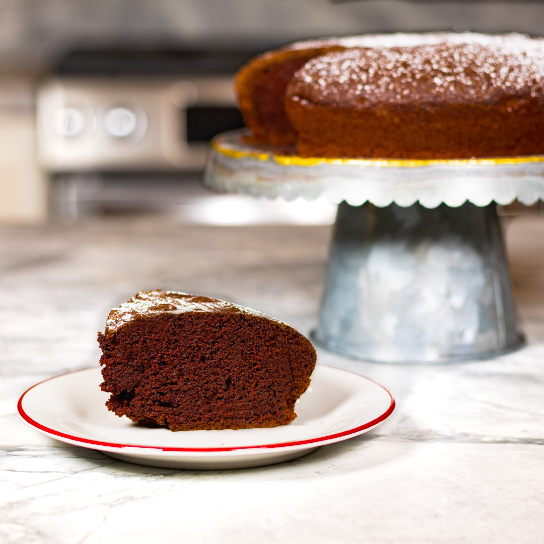 Chocolate Lemon Olive Oil Cake recipe resting on cake stand with one slice plated 