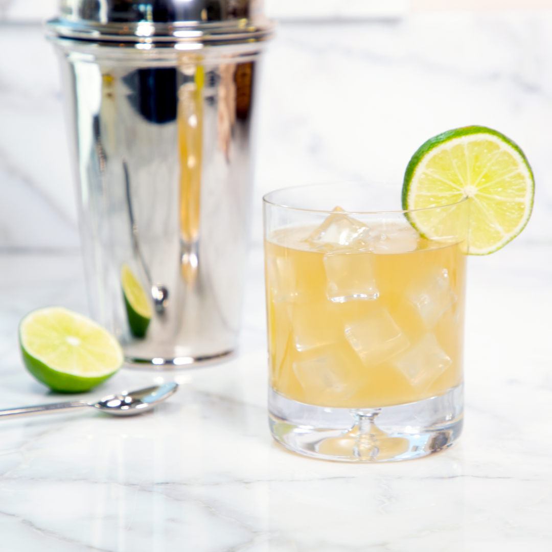 Pasolivo Spicy Pineapple Margarita Recipe garnished with a lime slice, next to a shaker and a fresh cut lime