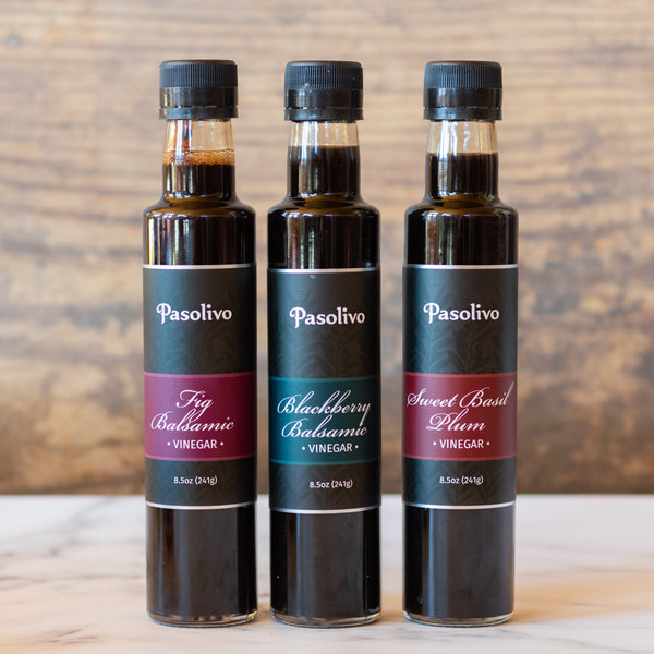 Three bottles of Pasolivo vinegar on a wooden surface with a wooden background